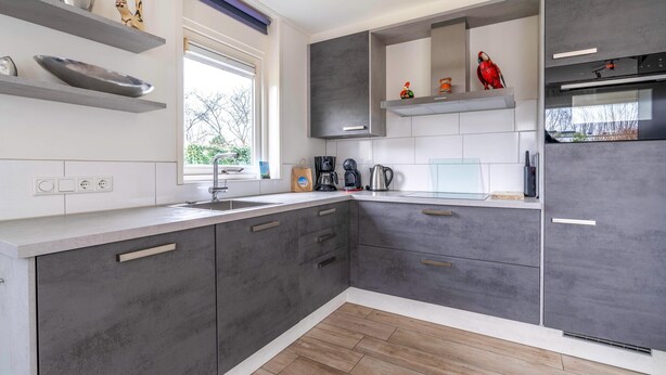 A modern kitchen with grey cabinets, a white countertop, and a window providing natural light. - Cozy and Comfortable 4-person Bungalow (De Koog)