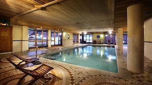 An indoor swimming pool with a tiled floor, wooden lounge chairs, and large windows. - Apartment in Savoy Near Ski Slopes (Bourg-Saint-Maurice)