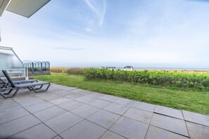 A patio with a view of the sea, a grassy area, and a building in the distance. - 2-person sea View Apartment With a Panoramic View Over the North Sea (De Koog)