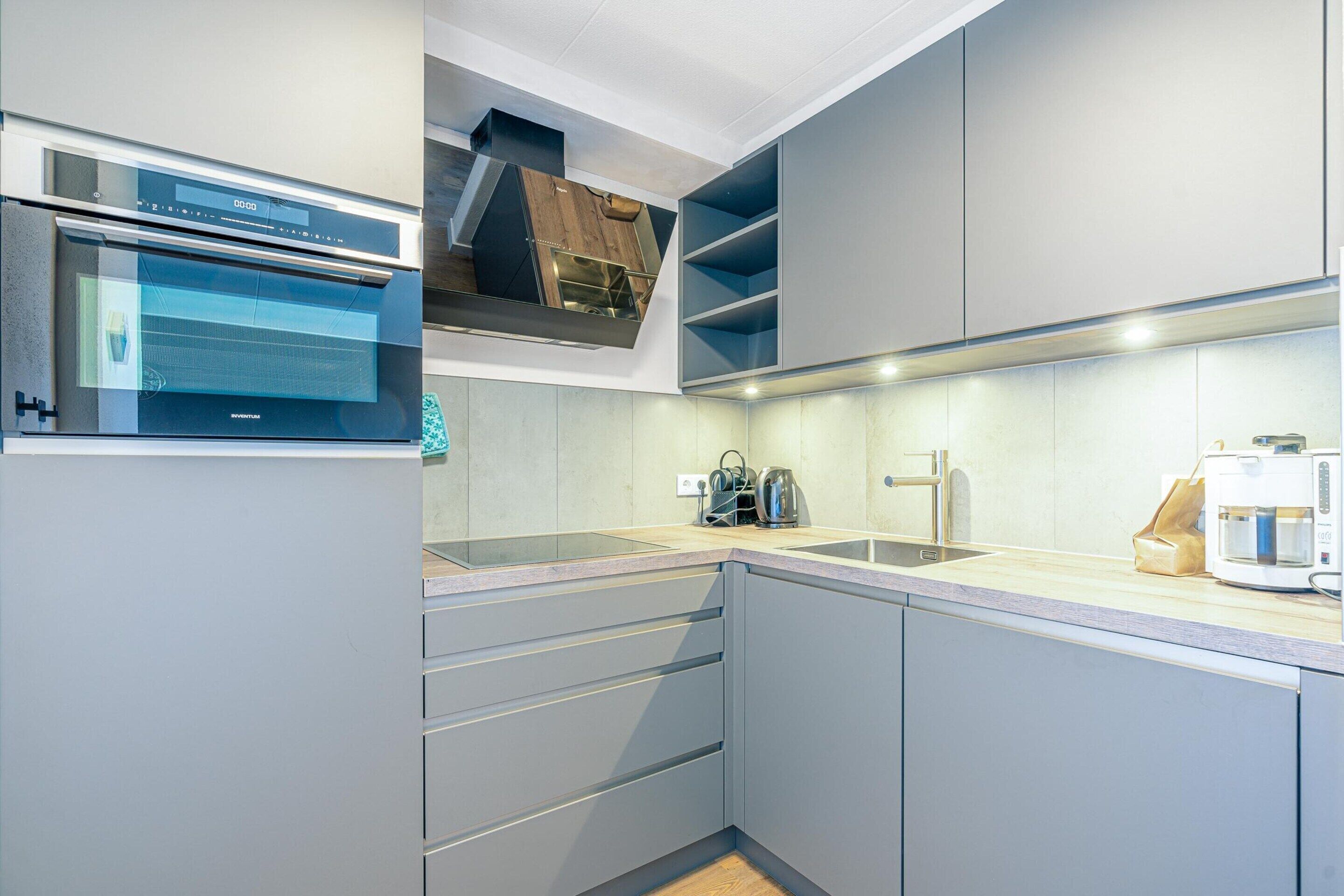 Een moderne keuken met grijze kastjes, een inbouwoven en een koffiezetapparaat.