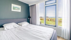 Een slaapkamer met een groot bed, een nachtkastje, een lamp en een raam met uitzicht op het strand.