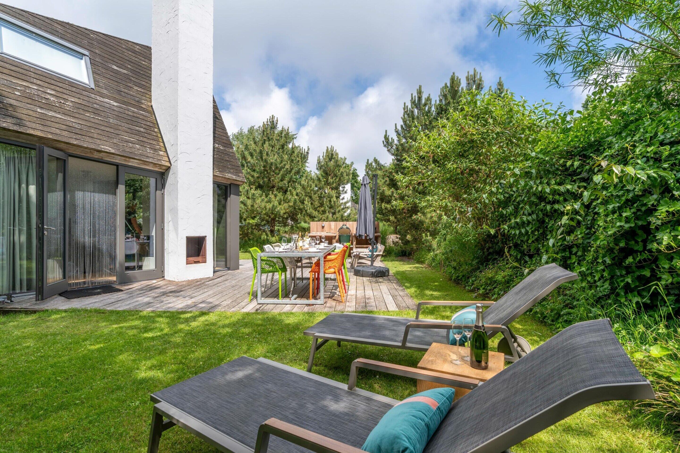 A modern outdoor patio with a dining table and chairs, a lounge area with two chairs, and a wooden deck.