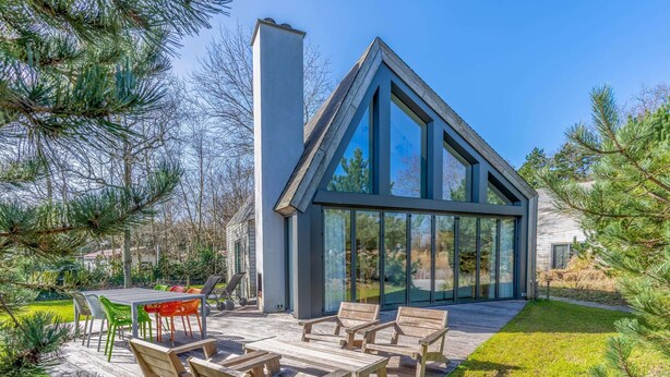 Une maison moderne dotée d’une grande façade vitrée, d’une terrasse en bois et d’un espace salon extérieur.