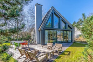 Une maison moderne dotée d’une grande façade vitrée, d’une terrasse en bois et d’un espace salon extérieur.