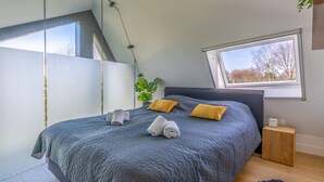 Une chambre à coucher avec un grand lit, deux oreillers, une table de chevet, une fenêtre et une plante.