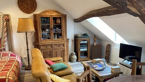 Un salon chaleureux de style loft, doté d’un haut plafond, de poutres apparentes, d’un canapé en cuir, d’un meuble en bois aux portes vitrées et d’un téléviseur.