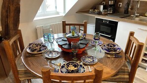 Une table de salle à manger ronde en bois, surmontée d’assiettes bleues et dorées, entourée de chaises en bois dotées de coussins à rayures.