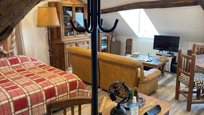 Une pièce mansardée accueillante, avec un lit, une malle en bois, une télévision et une table à manger.