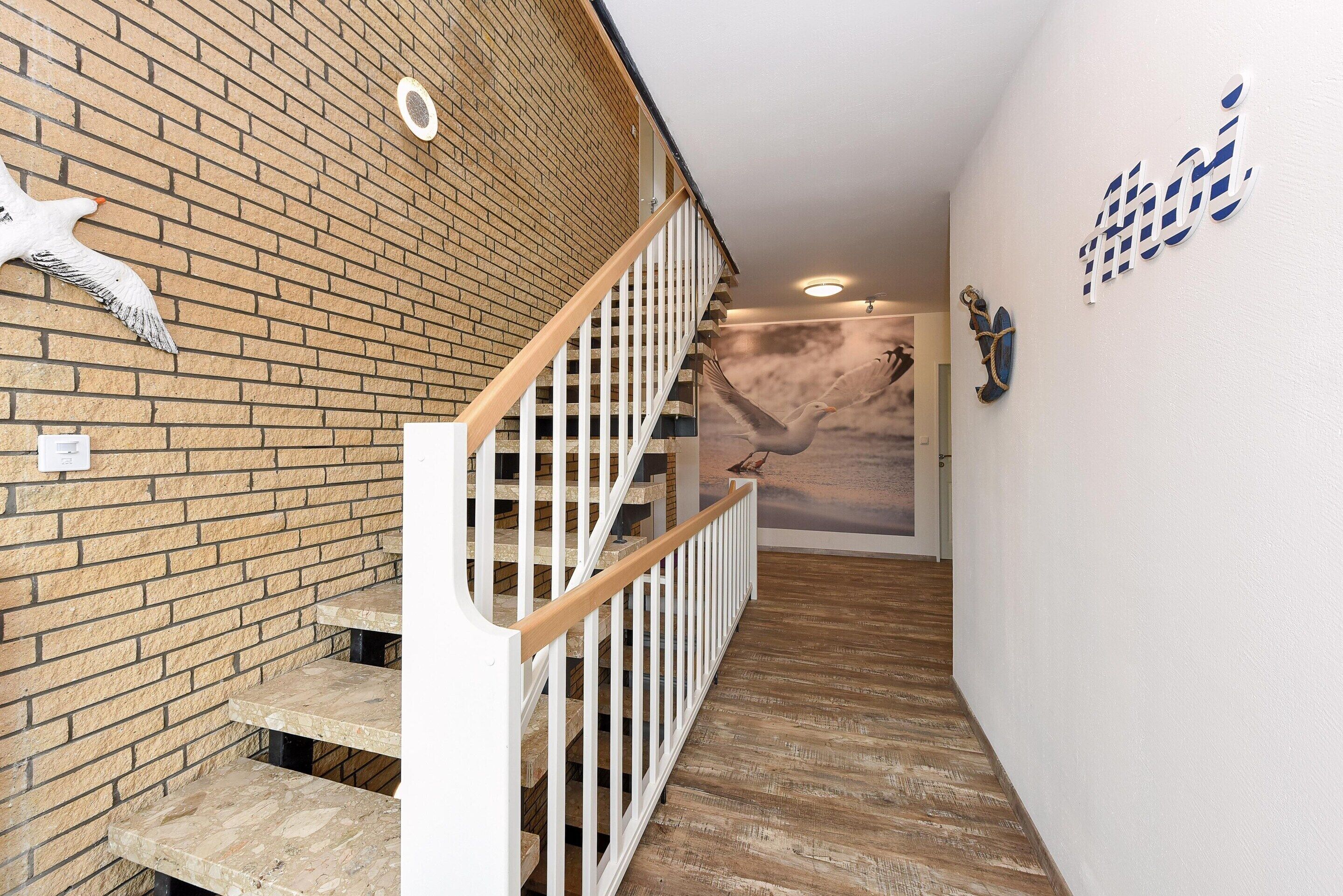 A staircase with a wooden handrail and white balusters, leading to a room with a brick wall and a mural of birds.