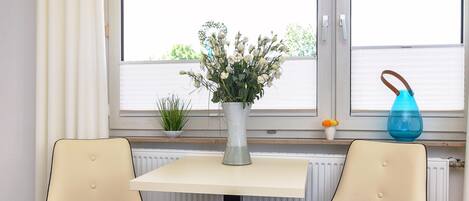 A room with a table and two chairs, a window with blinds, a radiator, and a small plant on the windowsill.