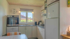 A compact kitchen with a built-in oven, a refrigerator, and a window with a view of a house and greenery. - 5 Star Holiday Home in Haarby (Haarby)