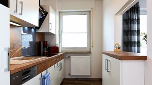 A narrow kitchen with a window, wooden countertop, white cabinets, and a built-in dishwasher. - Ferienwohnung in Bensersiel, 300 m vom Strand Entfernt (Esens)