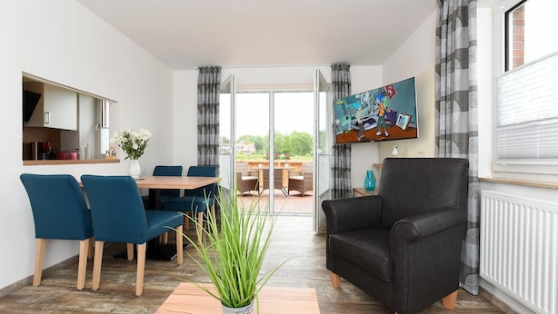 A modern living room with a dining area, a black leather sofa, and a TV on the wall. - Ferienwohnung in Bensersiel, 300 m vom Strand Entfernt (Esens)