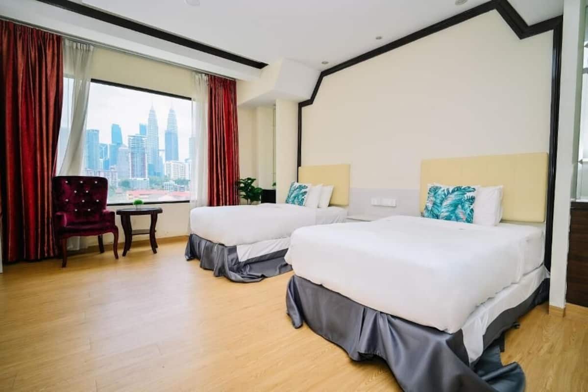 A hotel room with two beds, a red chair, a small table, and a city view.