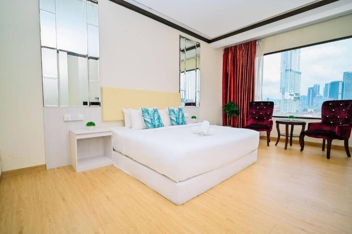 A modern hotel room with a large bed, a small desk, a chair, and a view of the city skyline.