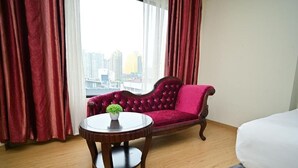 A hotel room with a red velvet sofa, a round wooden table with a plant, and a bed. - Kingston Hotel 5 at Chow Kit (Kuala Lumpur)