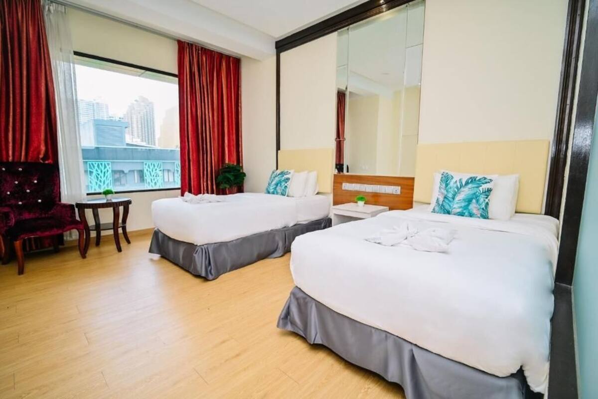 A hotel room with two beds, a desk, a chair, and a large window with curtains.