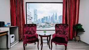 A room with two plush red chairs, a small round table, and a view of a city skyline through a large window. - Kingston Hotel 5 at Chow Kit (Kuala Lumpur)