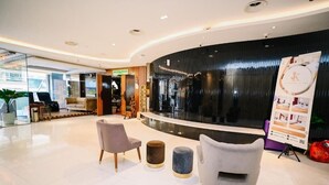 A modern lobby with a curved reception desk, seating area with chairs and ottomans, and a glass wall offering a view of the outside. - Kingston Hotel 5 at Chow Kit (Kuala Lumpur)