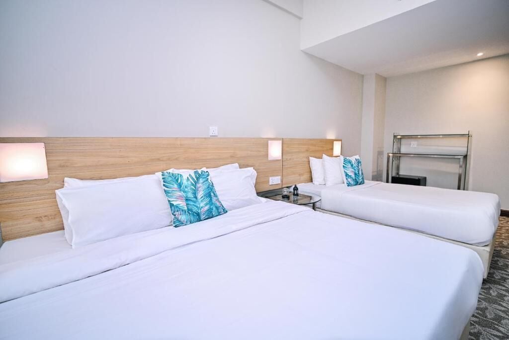 A hotel room with two beds, a wooden headboard, bedside lamps, a small table, and a built-in TV.