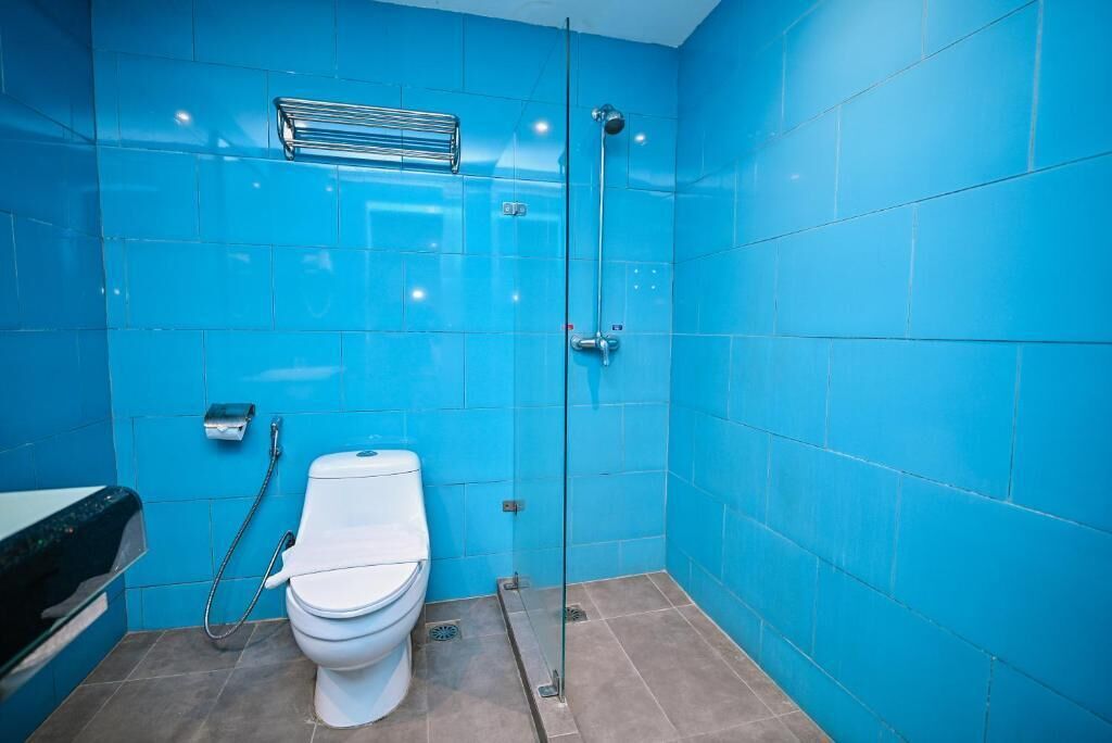 Une salle de bain avec des carreaux bleus, des toilettes blanches, une cabine de douche en verre et un porte-serviettes.
