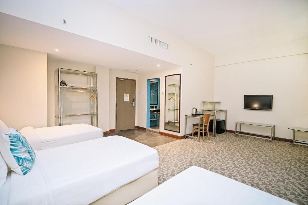 A hotel room with two beds, a desk, a chair, a TV, and a wardrobe.