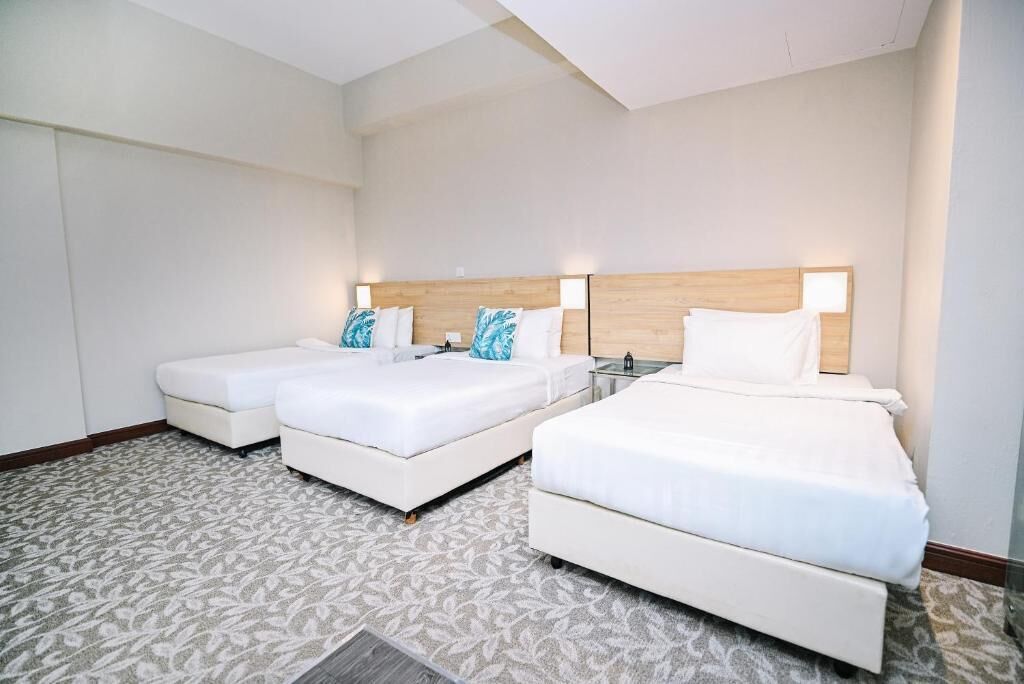 Habitación de hotel con dos camas individuales y una cama doble, todas con ropa de cama blanca y almohadones decorativos.