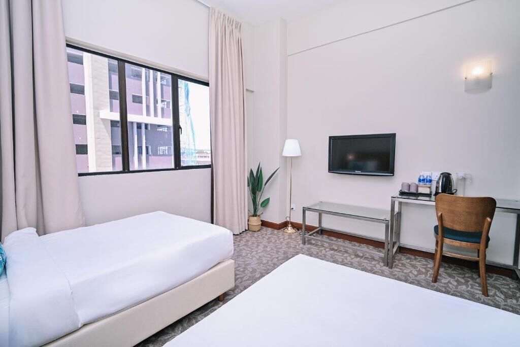 Habitación de hotel con dos camas, un escritorio con televisor, una silla y una ventana con cortinas.