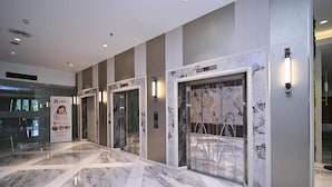 Un moderno vestíbulo de hotel con suelo de mármol, puertas de cristal y un ascensor panorámico.