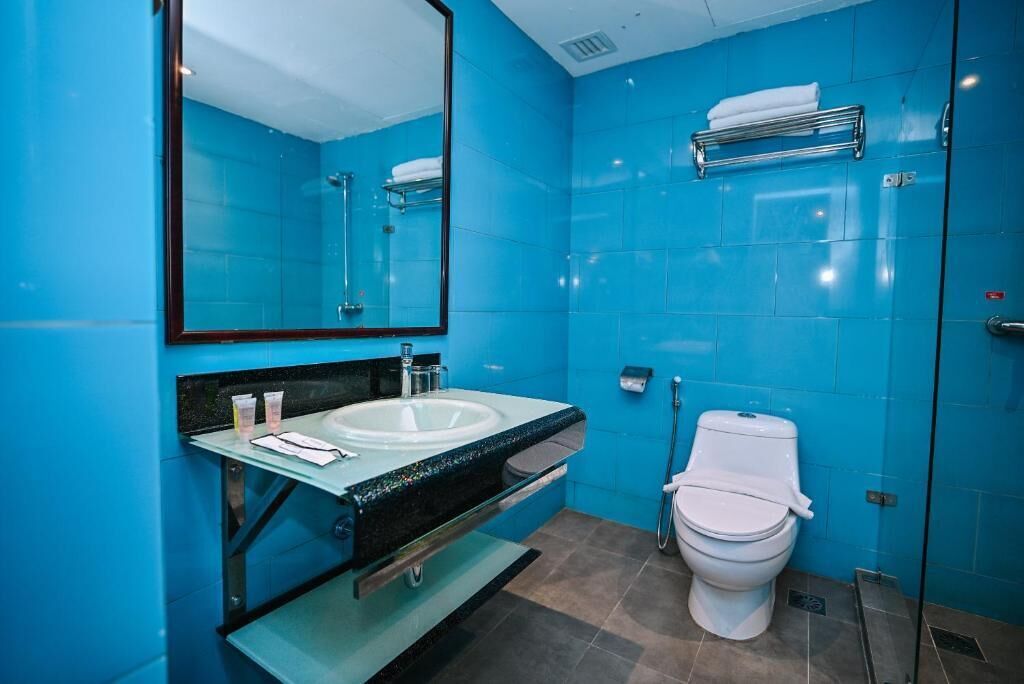 A bathroom with a blue tiled wall, a white sink, a mirror, a toilet, and a shower area.