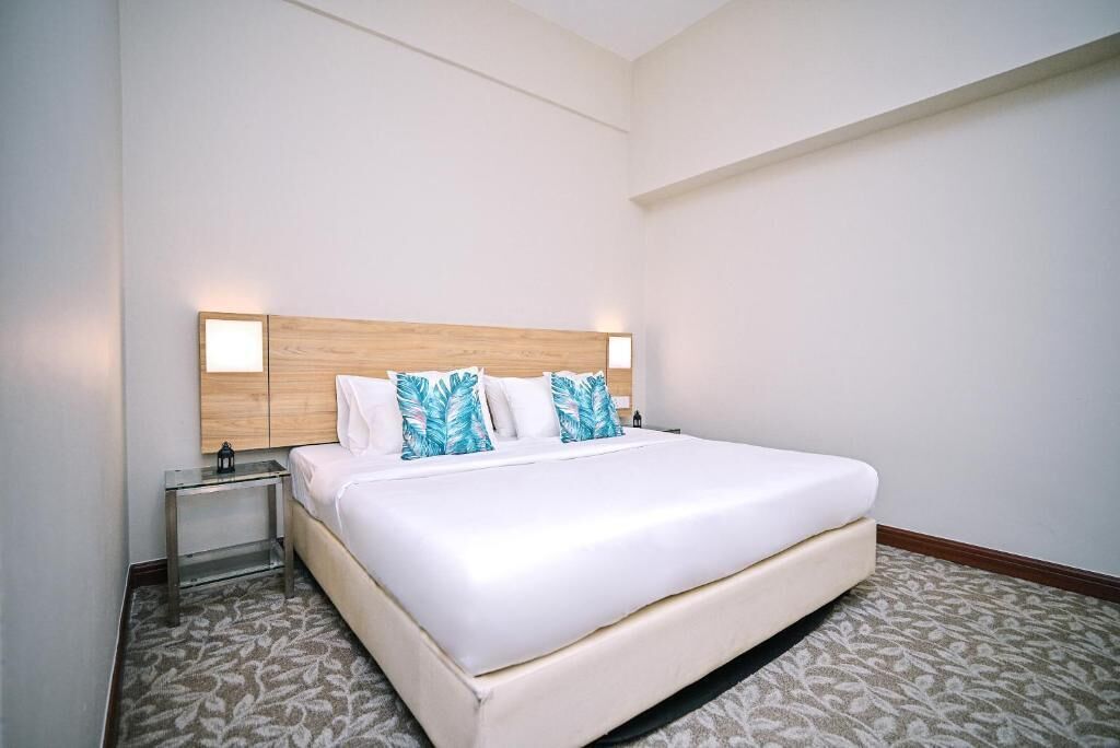 A hotel room with a large bed, a wooden headboard, two bedside tables, and a patterned carpet.