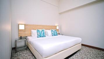 A hotel room with a large bed, a wooden headboard, two bedside tables, and a patterned carpet.