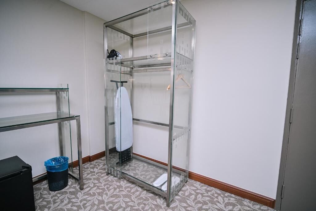A small, enclosed closet with glass doors, a metal shelf, and a blue trash bin.