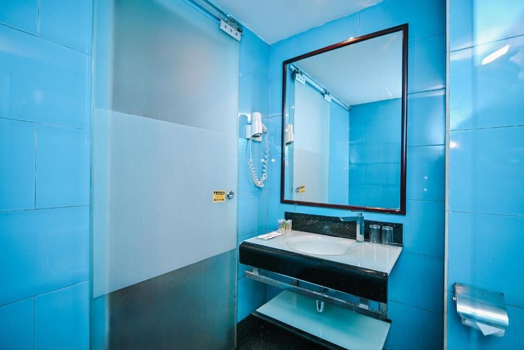 A bathroom with blue walls, a black sink, a mirror, and a hand dryer.
