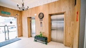 Eine Lobby mit Holzwandverkleidung, einer Uhr, zwei Aufzügen und einem kleinen Topf mit Grünpflanzen.