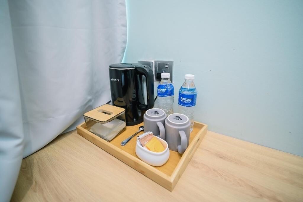 A wooden tray with a coffee maker, two water bottles, two mugs, a spoon, and a small container with a yellow item.