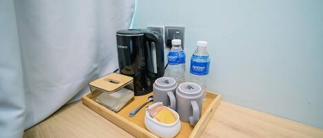 A wooden tray with a coffee maker, two water bottles, two mugs, a spoon, and a small container with a yellow item.