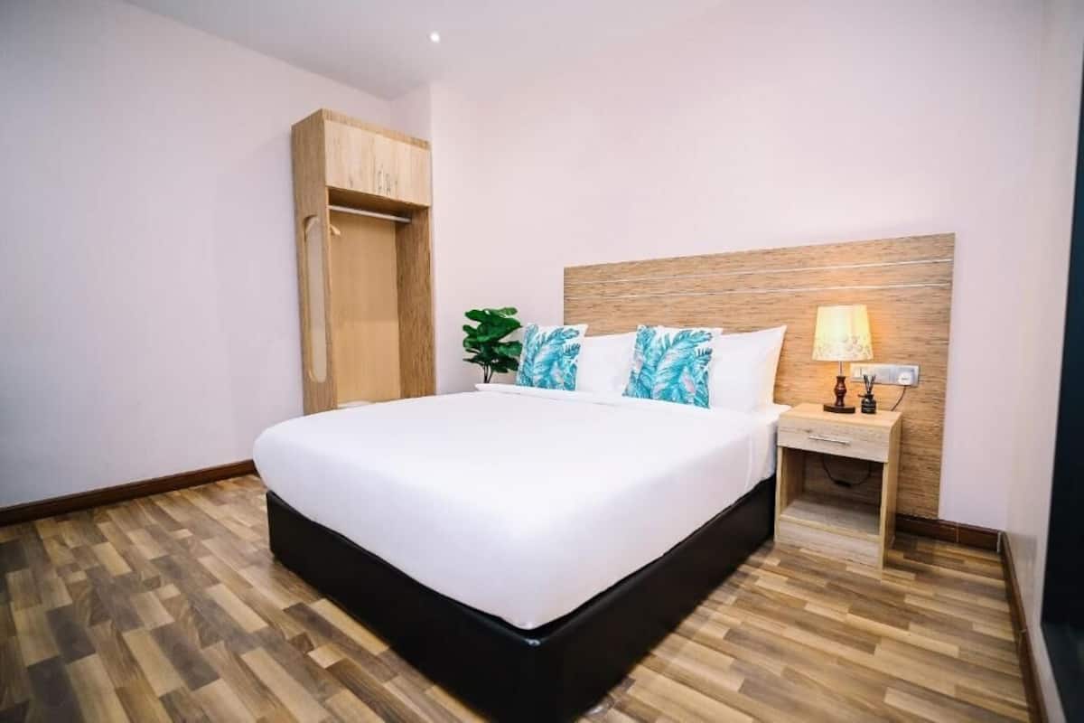 Un dormitorio con una cama grande, cabecera de madera, mesita de noche con lámpara y un armario.