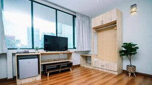 Ein modernes Wohnzimmer mit großem Fenster, Holzmöbeln, einem Flachbildfernseher und einem kleinen Kühlschrank.