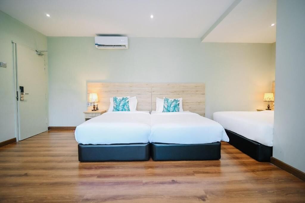 Habitación de hotel con dos camas, piso de madera, ventilador de techo y aire acondicionado instalado en la pared.