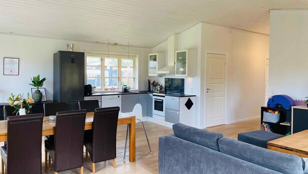 A modern kitchen with white cabinets, a dining table with chairs, and a grey sofa in a spacious living area.