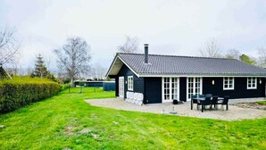 A black house with a tiled roof, a chimney, and a paved patio with outdoor furniture.