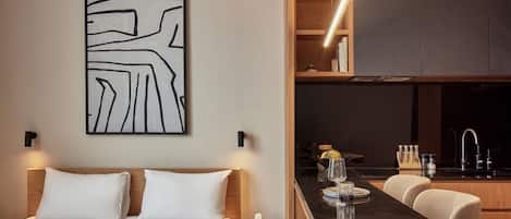 A modern hotel room with a bed, a small kitchenette, and a dining area.