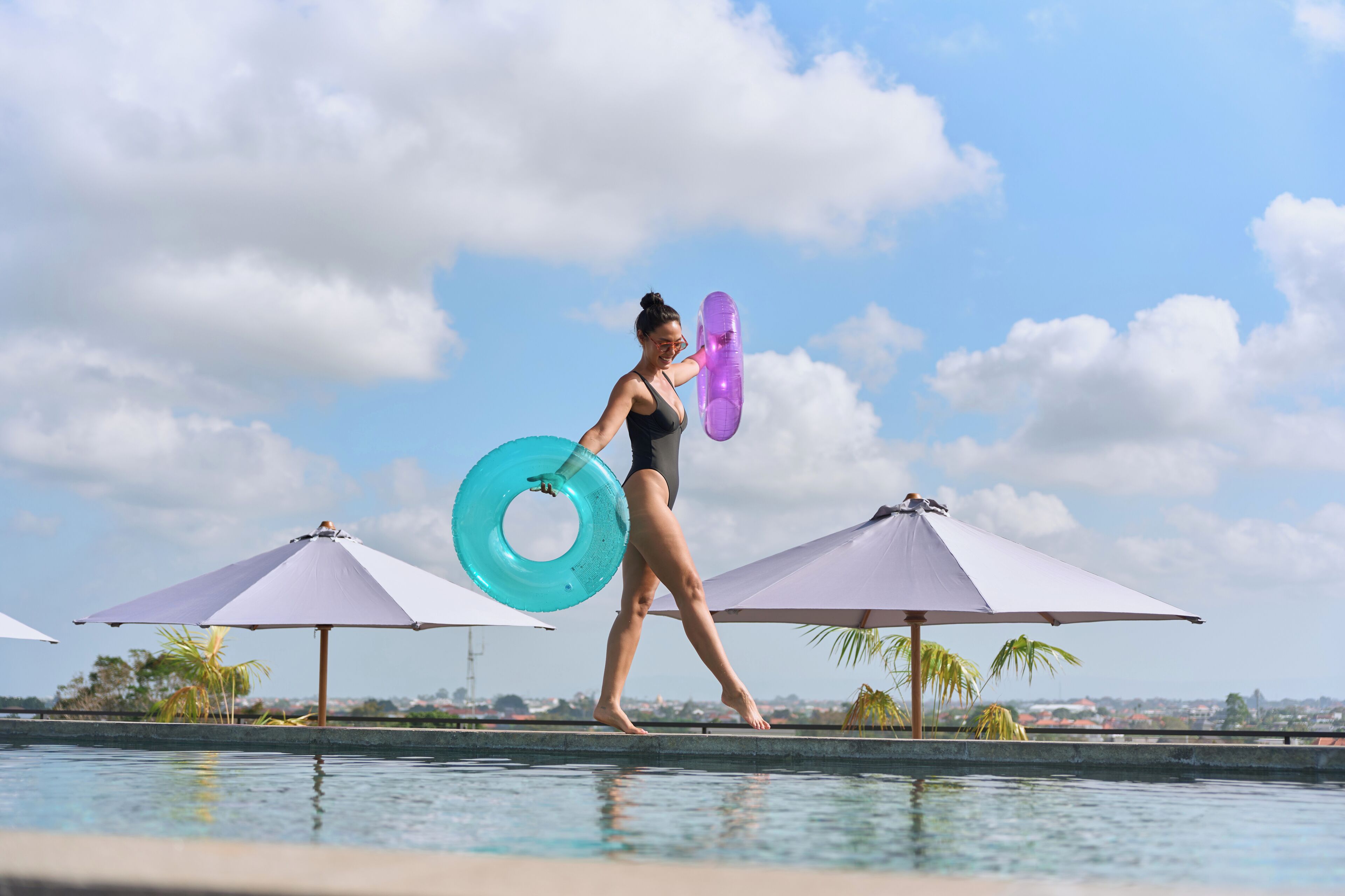 A person walking by a pool with umbrellas and a clear sky.