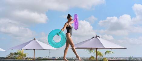 A person walking by a pool with umbrellas and a clear sky.