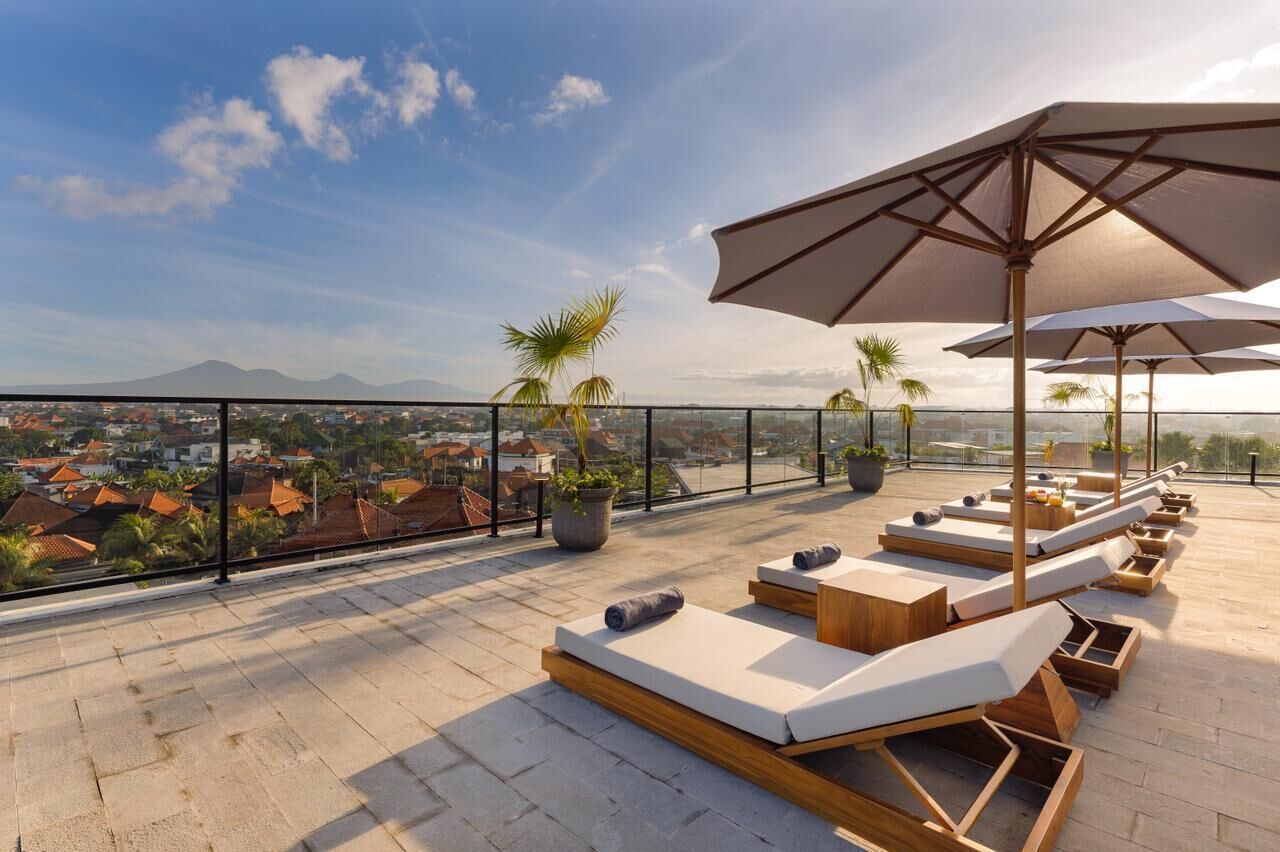 A rooftop terrace with sun loungers, umbrellas, and potted plants.