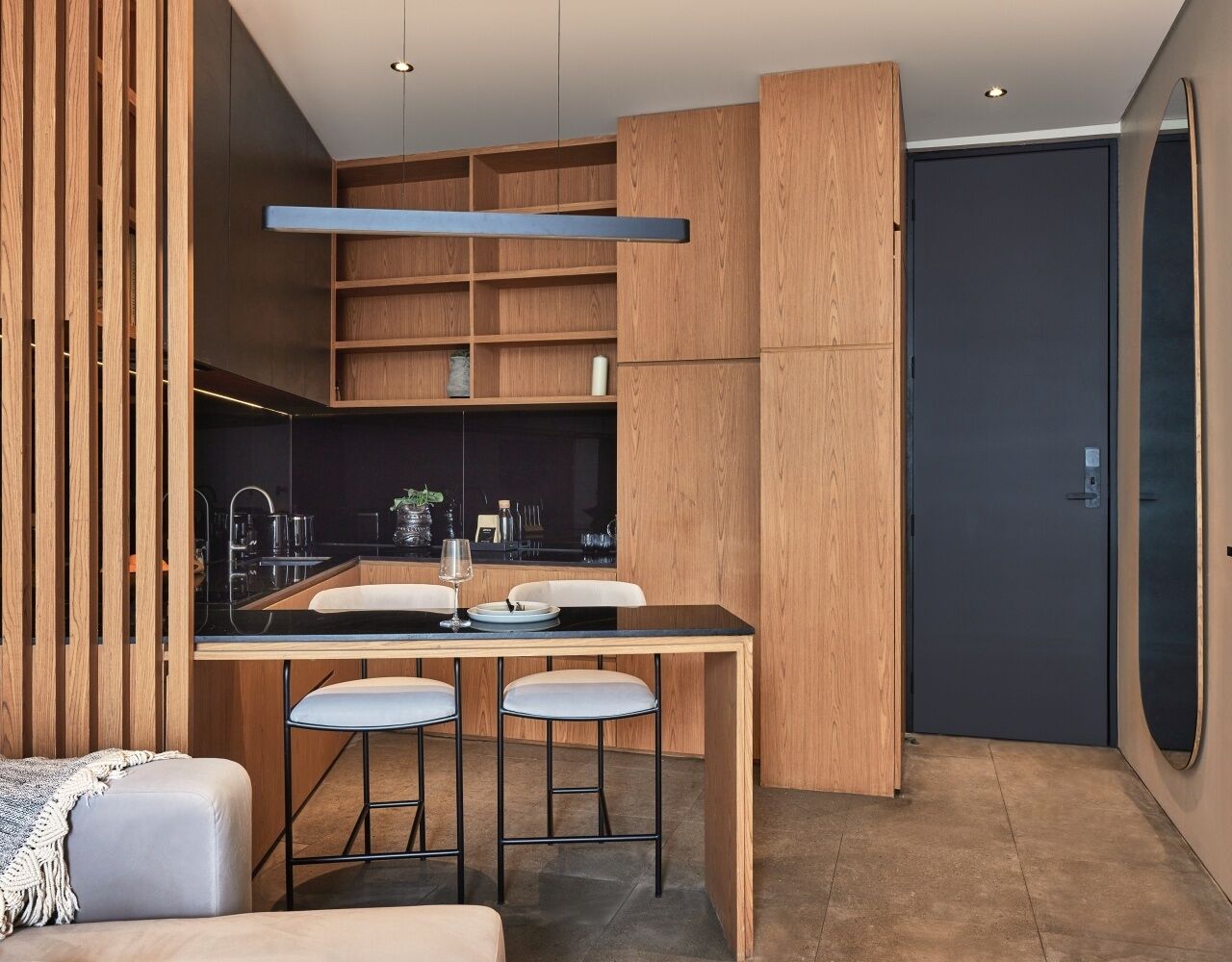 A modern kitchen with wooden cabinetry, a black countertop, and bar stools.