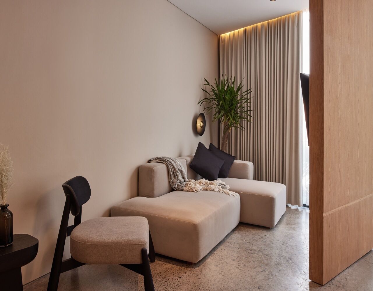 A modern living room with a beige sofa, a small side table, a black chair, and a potted plant.