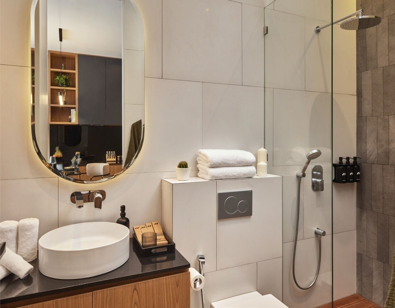 Une salle de bain moderne avec un grand miroir rond, un lavabo blanc, une douche et un meuble-lavabo doté d’une armoire en bois.