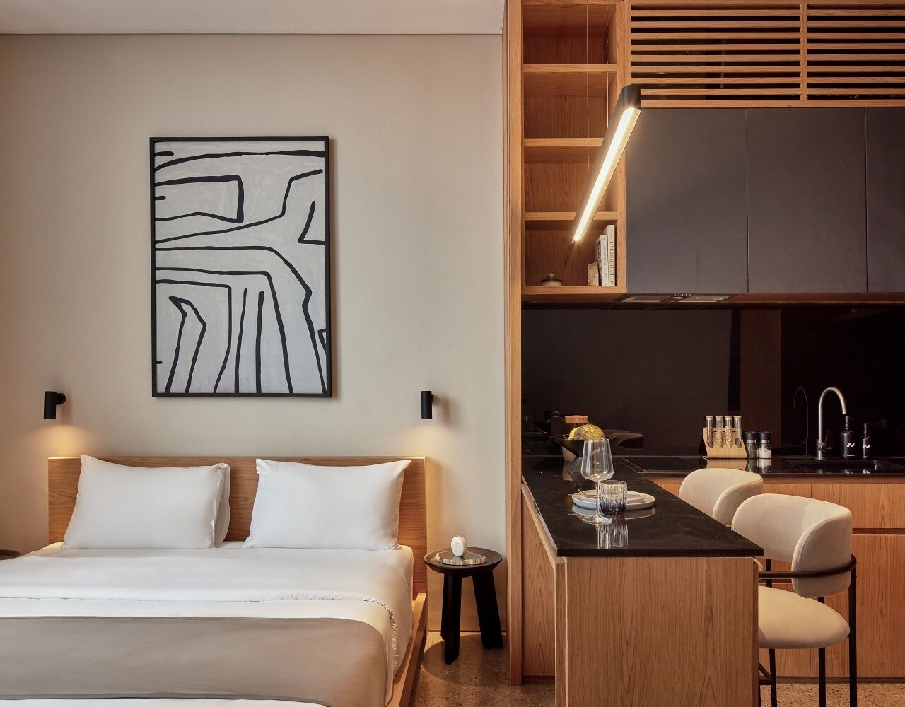Een moderne hotelkamer met een bed, nachtkastje en een klein kitchenette.